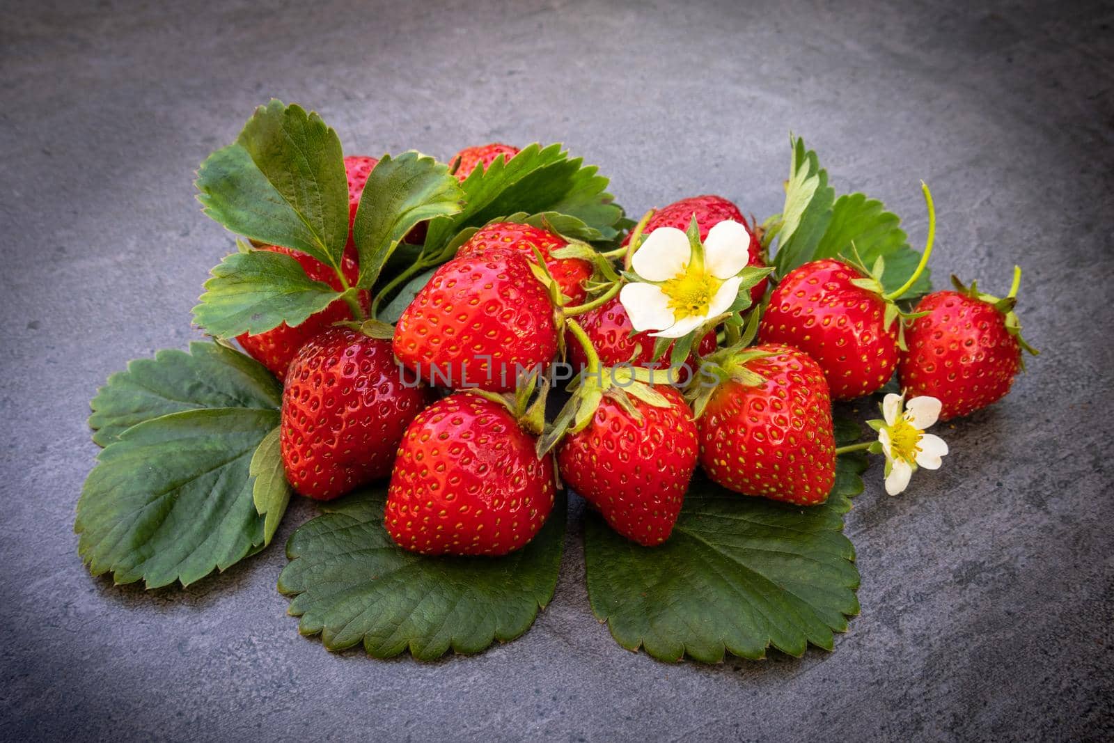 Red ripe strawberries with leaves over dark background