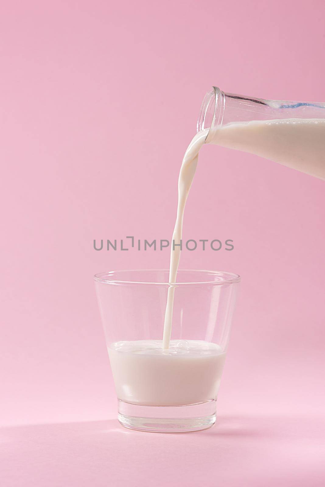 Pouring milk in to glass from bottle on a pink