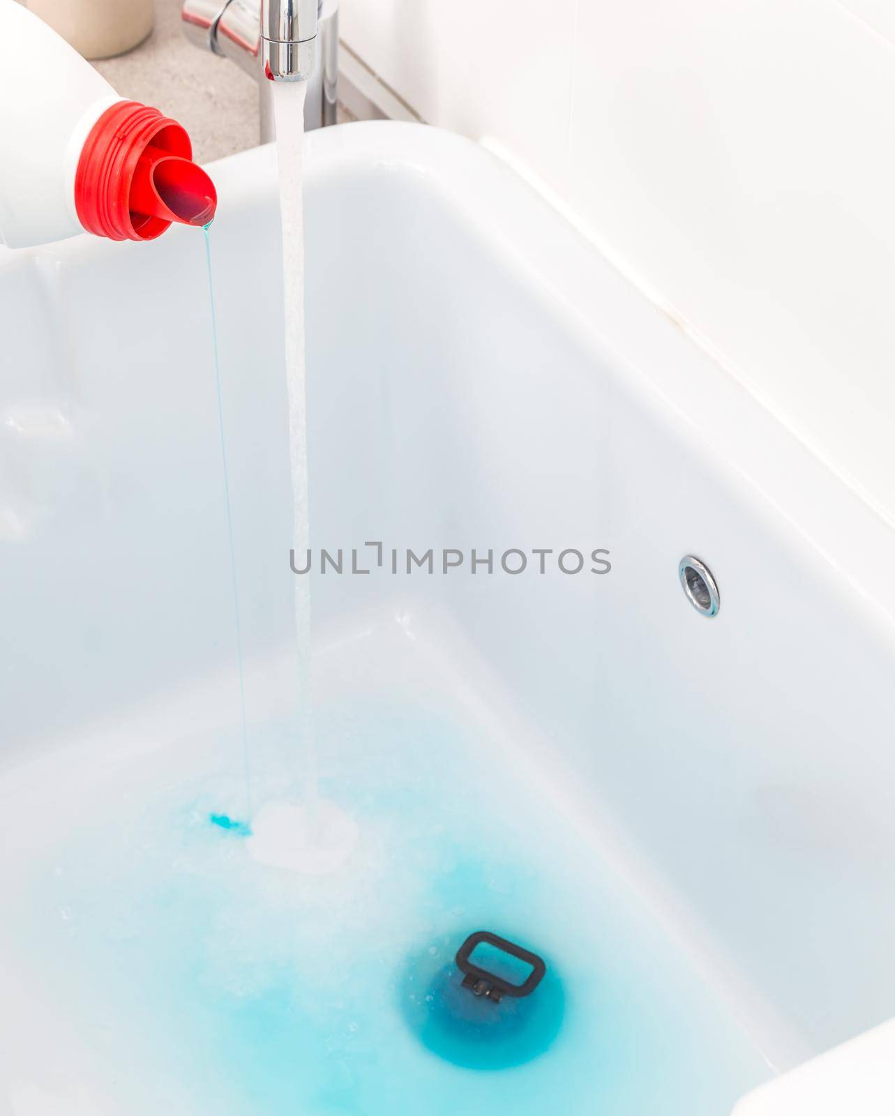 Pouring blue detergent into empty sink before washing clothes in laundry room by Mariakray