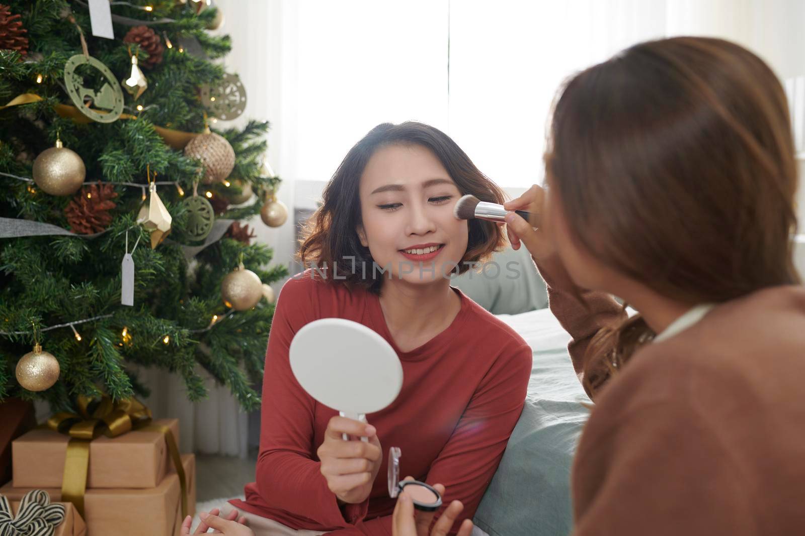 Creative young woman applying make-up on friend's face in sitting room by makidotvn