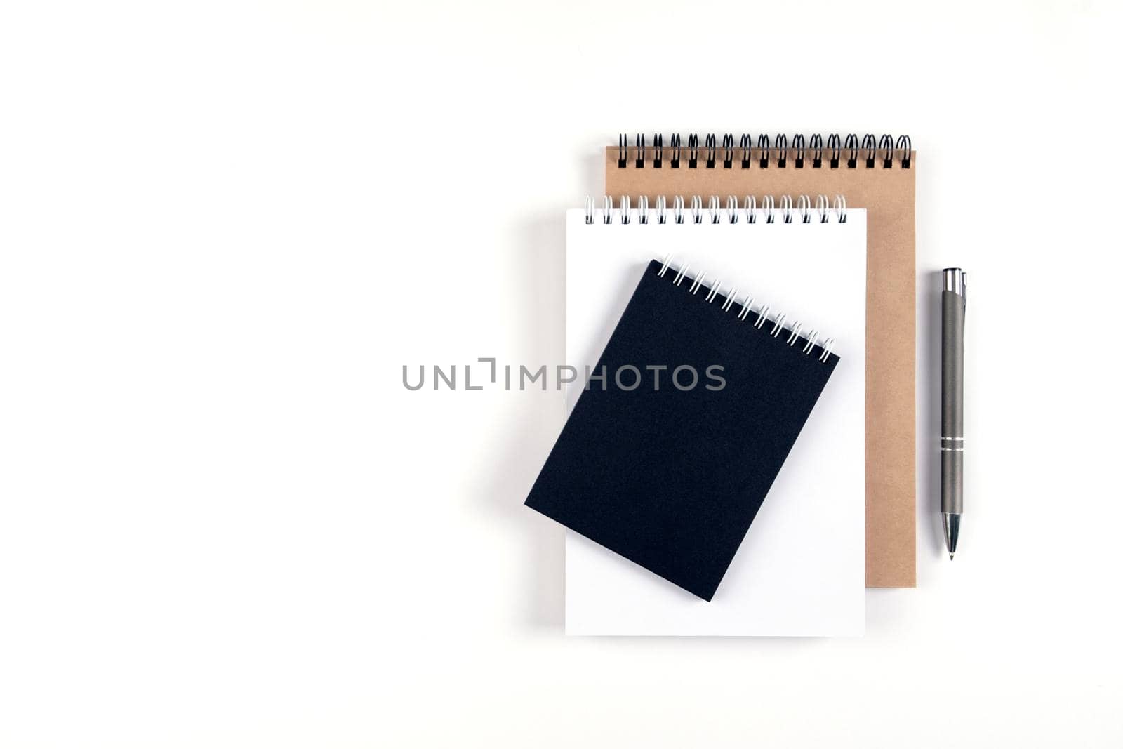 Three blank notepads on a spiral stacked in a stack on a white background. Notebooks with white, black and recycled sheets and pen. Education, office.