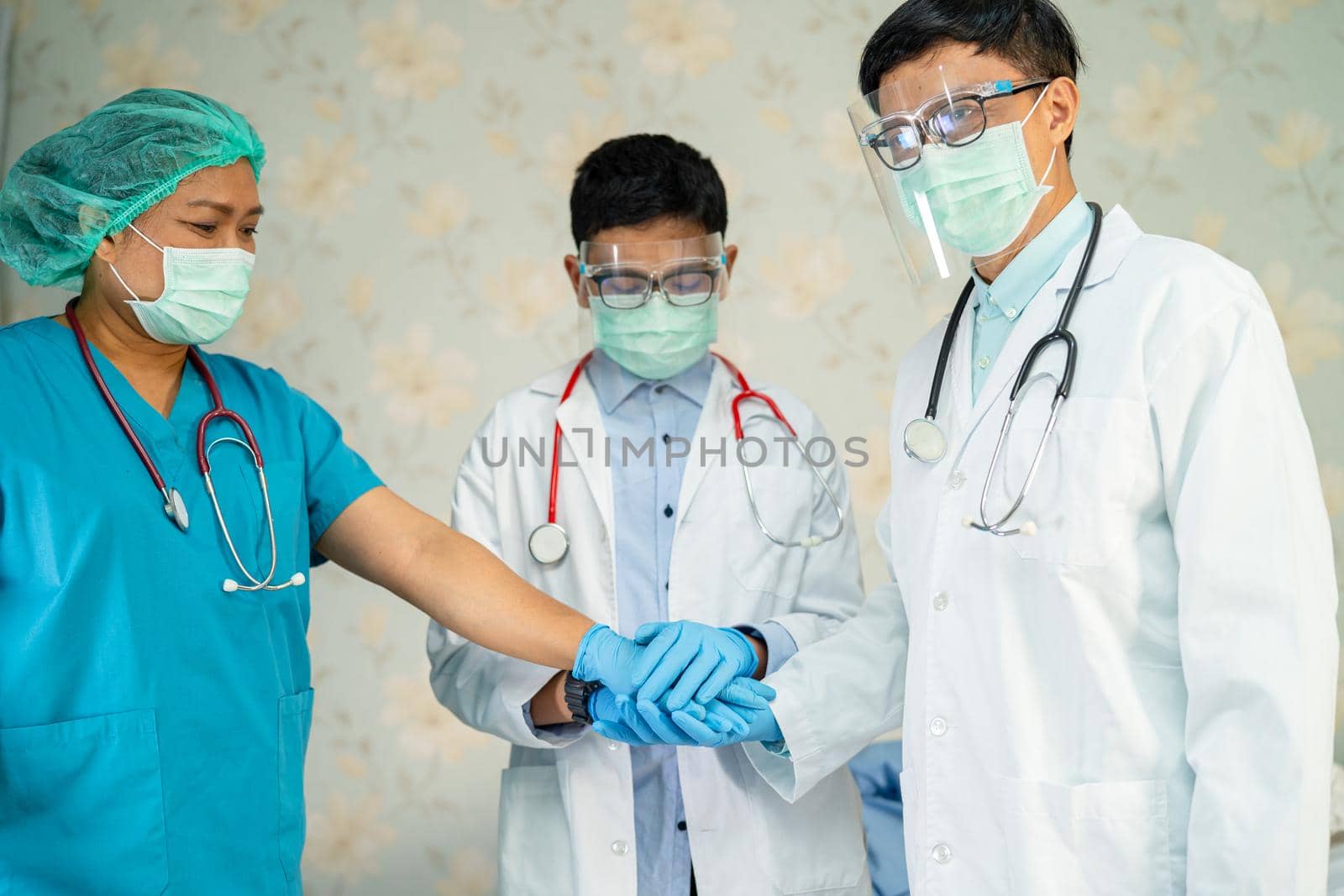 Asian doctor team stack hands together as team for motivation new normal to treat infection Covid-19 Coronavirus at hospital ward. by pamai