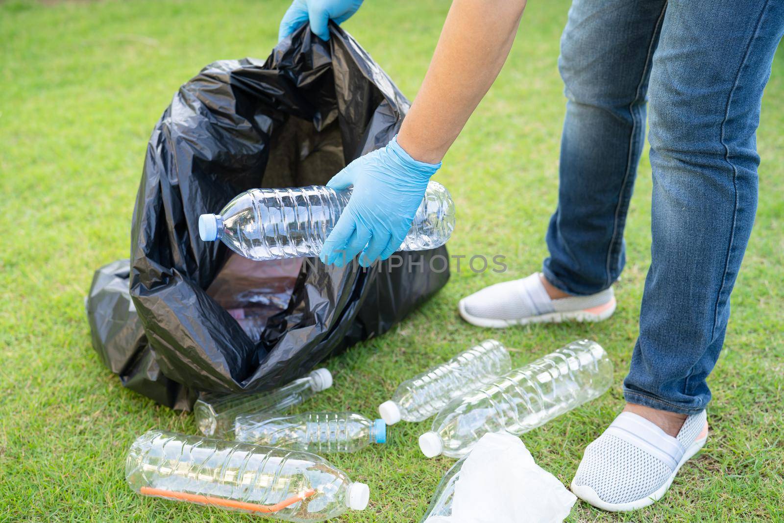 Asian woman volunteer carry water plastic bottles into garbage bag trash in park, recycle waste environment ecology concept.