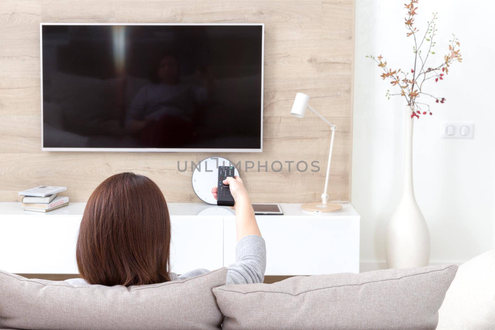 Young woman watching TV in the living room. Back view