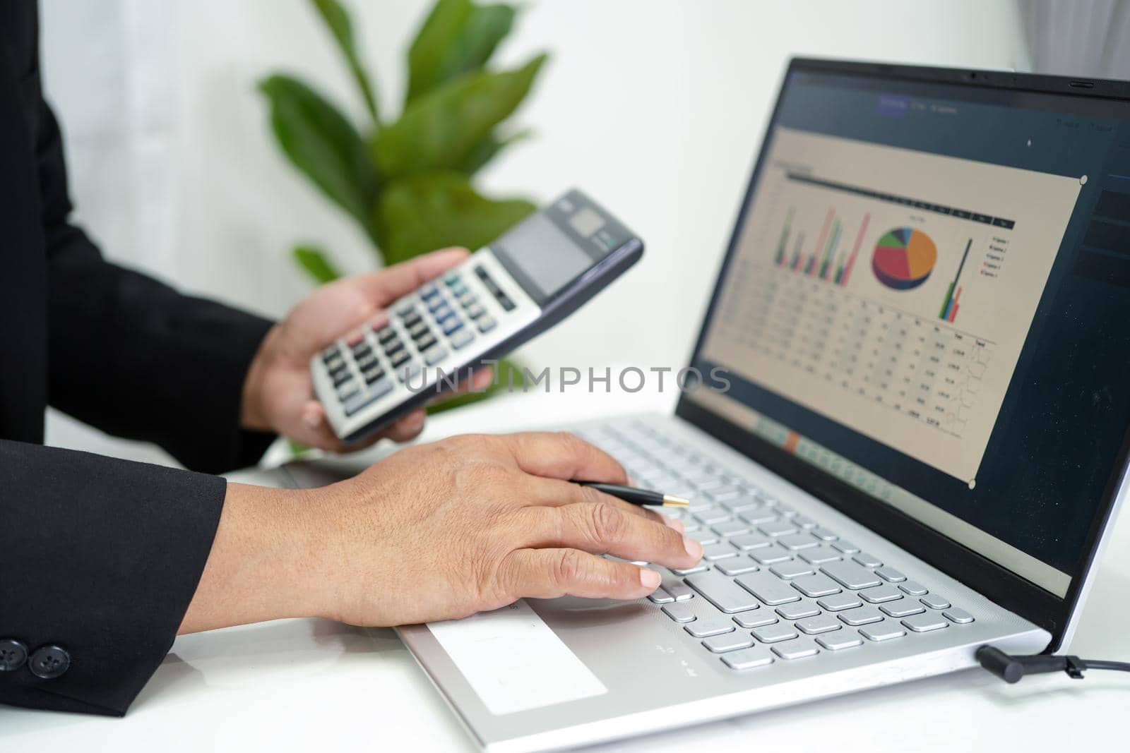 Asian accountant working and analyzing financial reports project accounting with chart graph in laptop and calculator in modern office, finance and business concept. by pamai