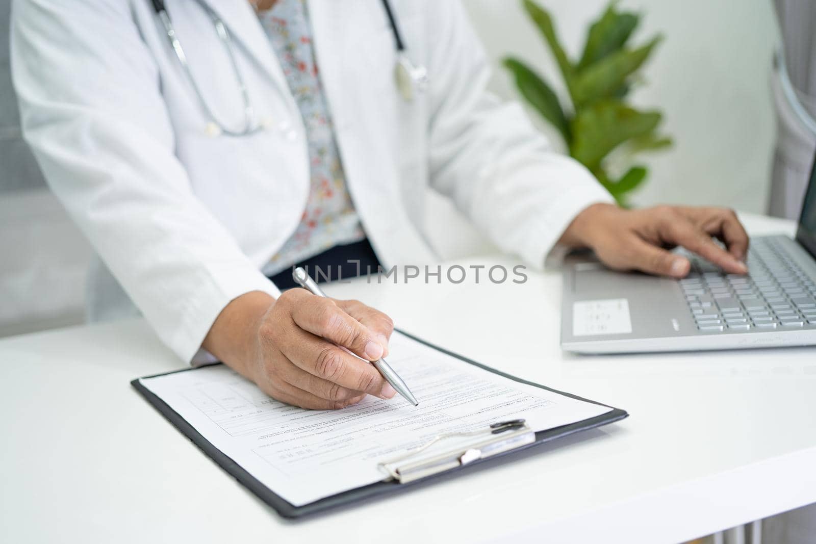 Doctor write health medical note in clipboard with laptop in hospital. by pamai