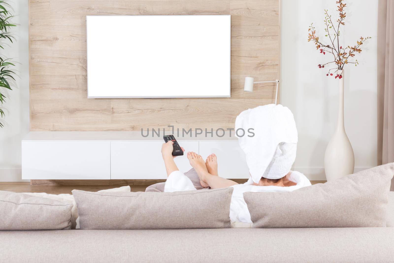 Woman sitting on couch with towel on her head watching tv. White screen for design