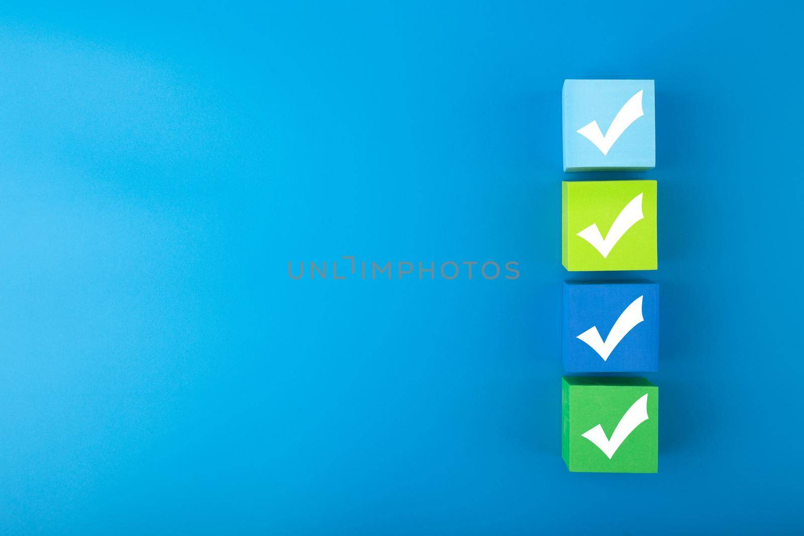Four checkmarks on colorful cubes against bright blue background with copy space. Minimal trendy concept of questionary, checklist, to do list, planning, business or verification