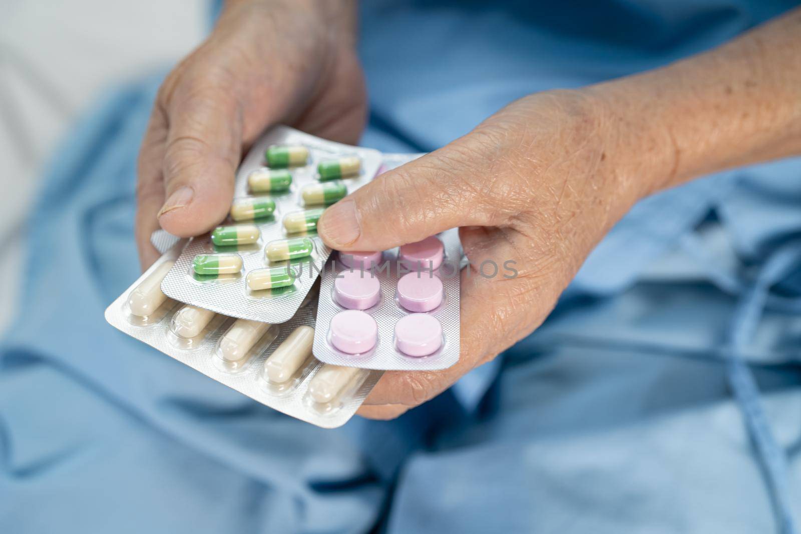 Asian senior or elderly old lady woman patient holding antibiotics capsule pills in blister packaging for treatment infection patient in hospital; Pharmacy drugstore concept. by pamai