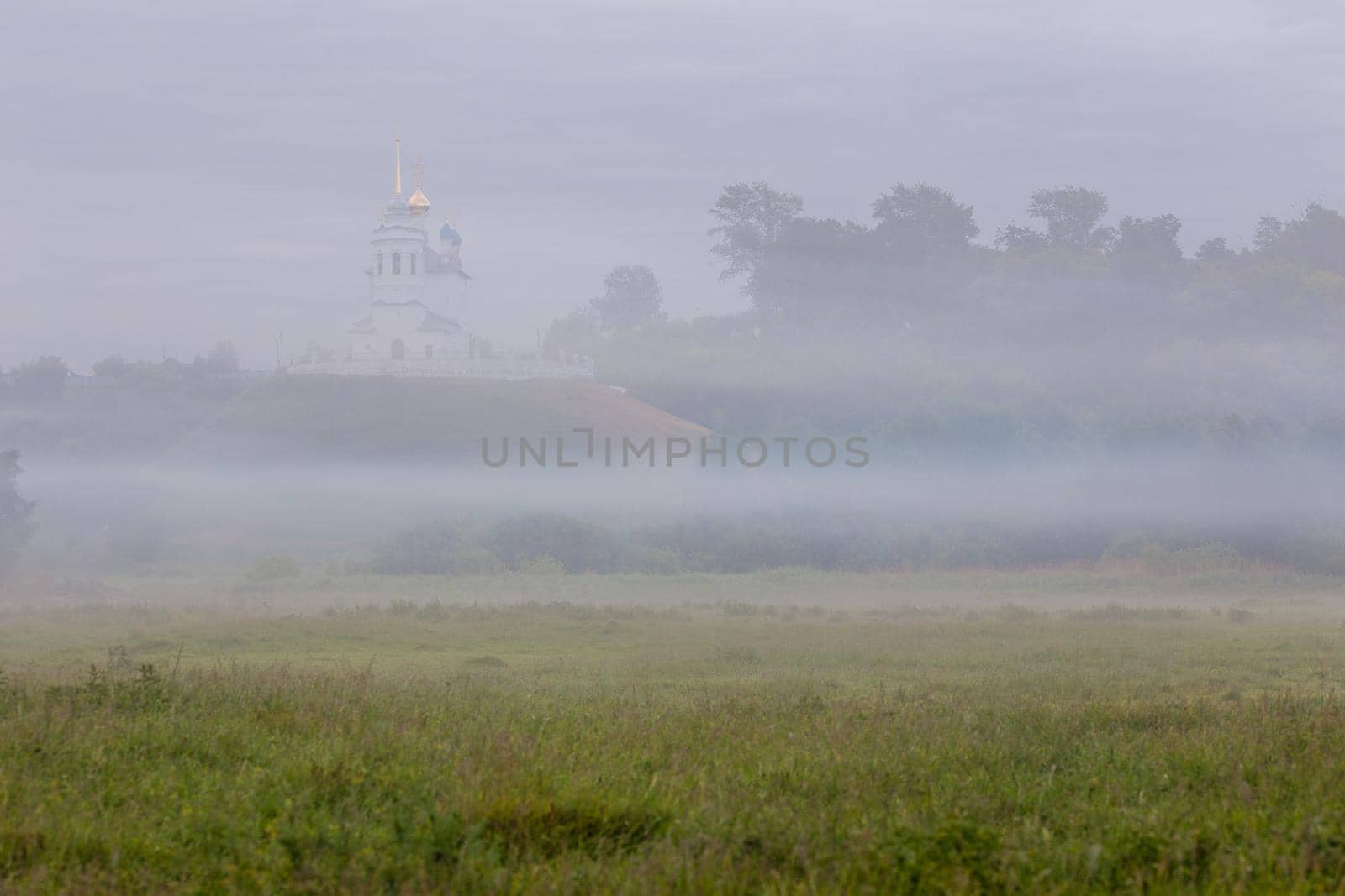 foggy summer morning landscape with the church on the hill in the background.