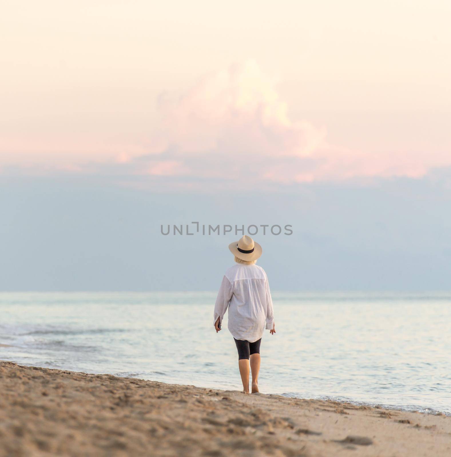 Woman wearing straw hat walking on beach at sunset
