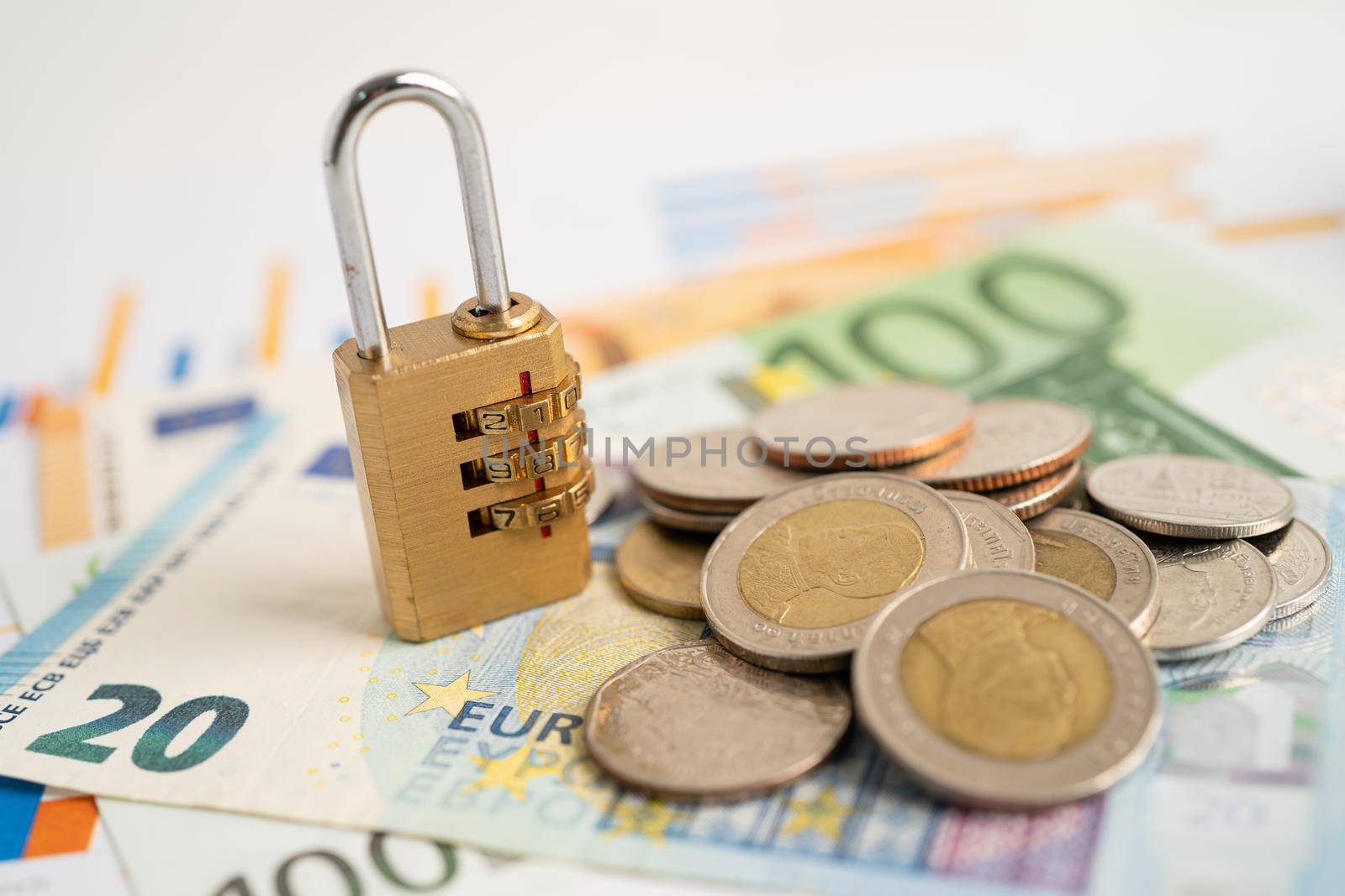 Golden security digital password lock key and coins with with Euro banknotes on graph, trade finance concept.