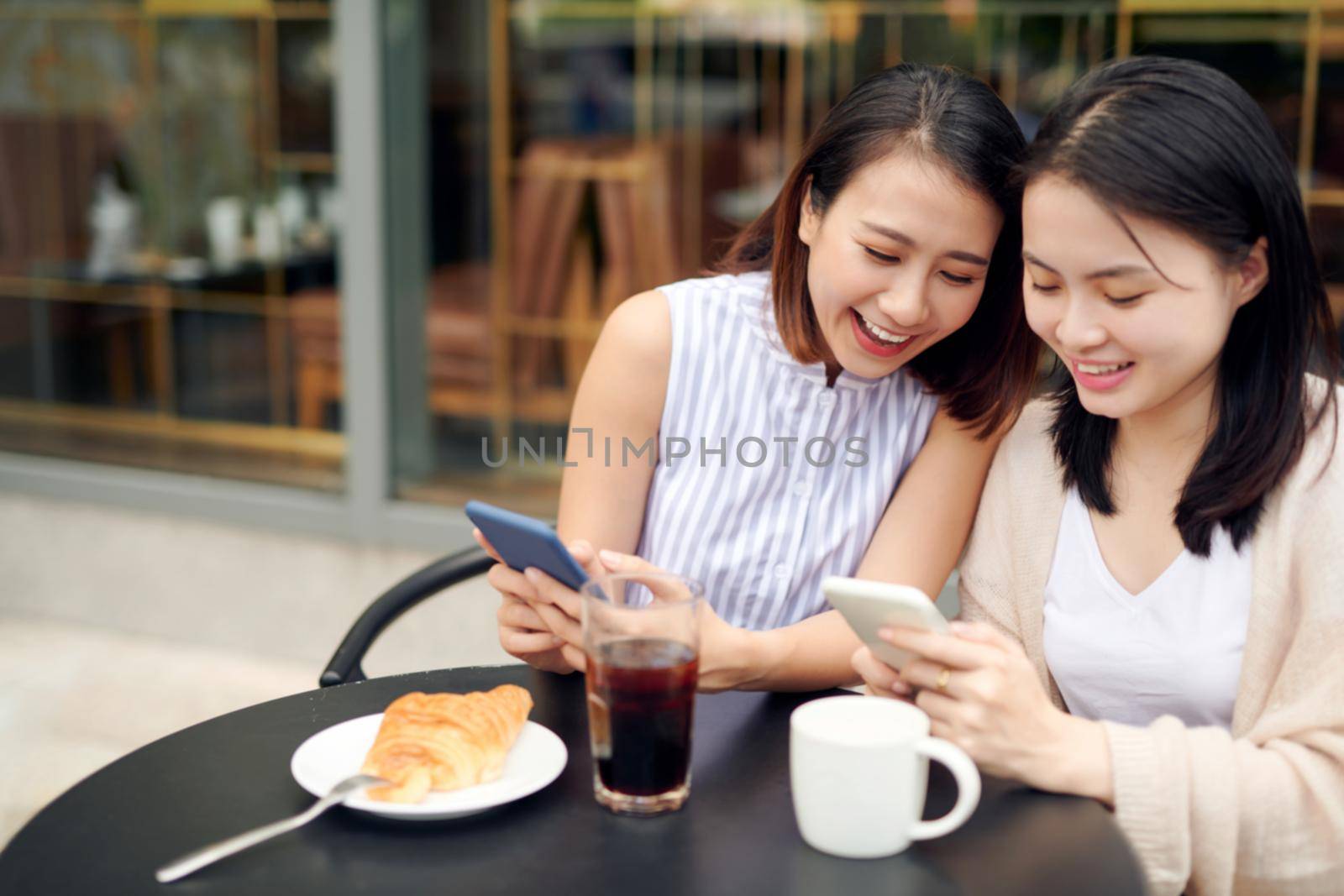 Happy girls using mobile in cafeteria.