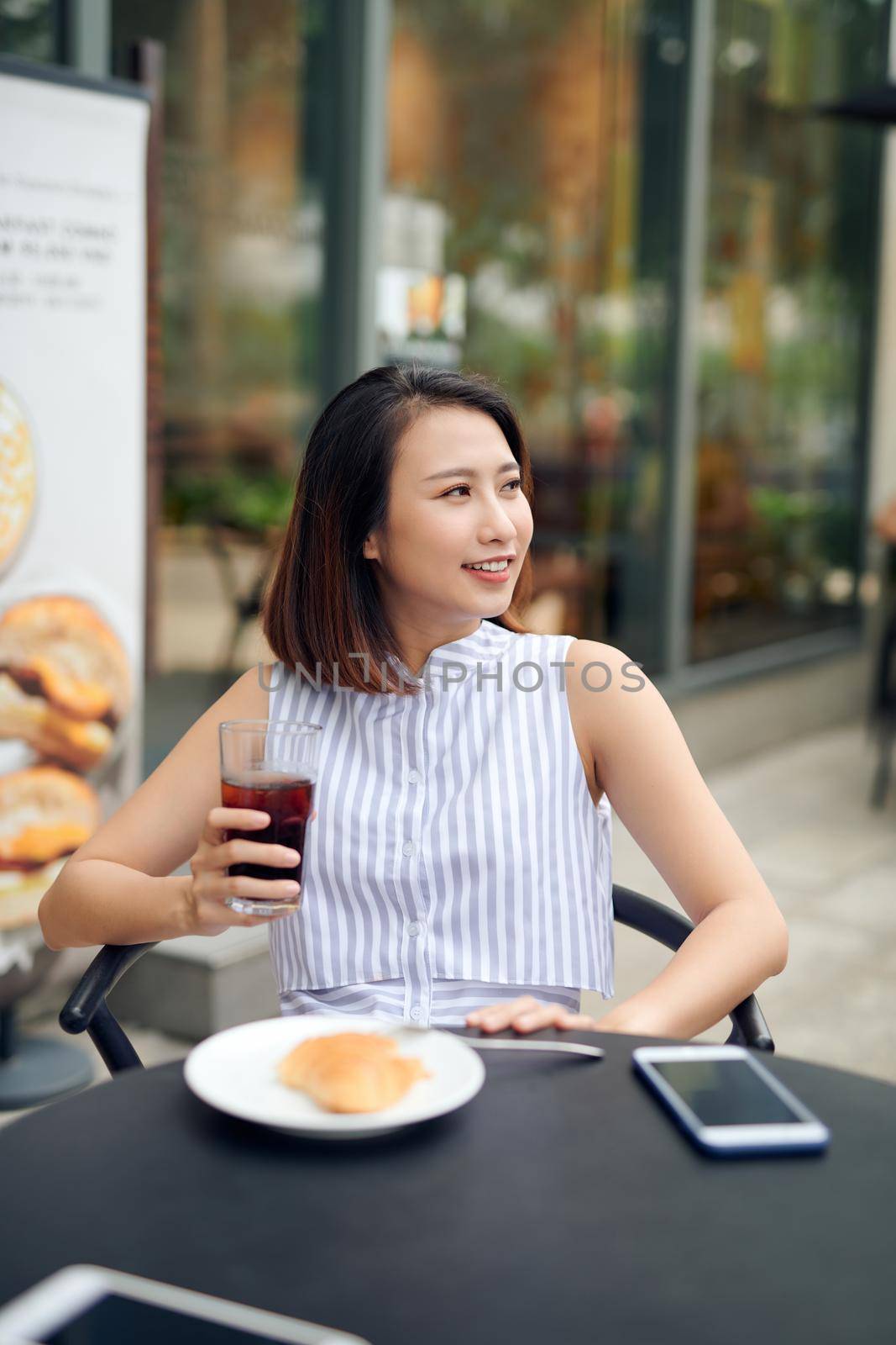 Young beautiful girl with cellphone drinking coffee in a cafe at a table by makidotvn