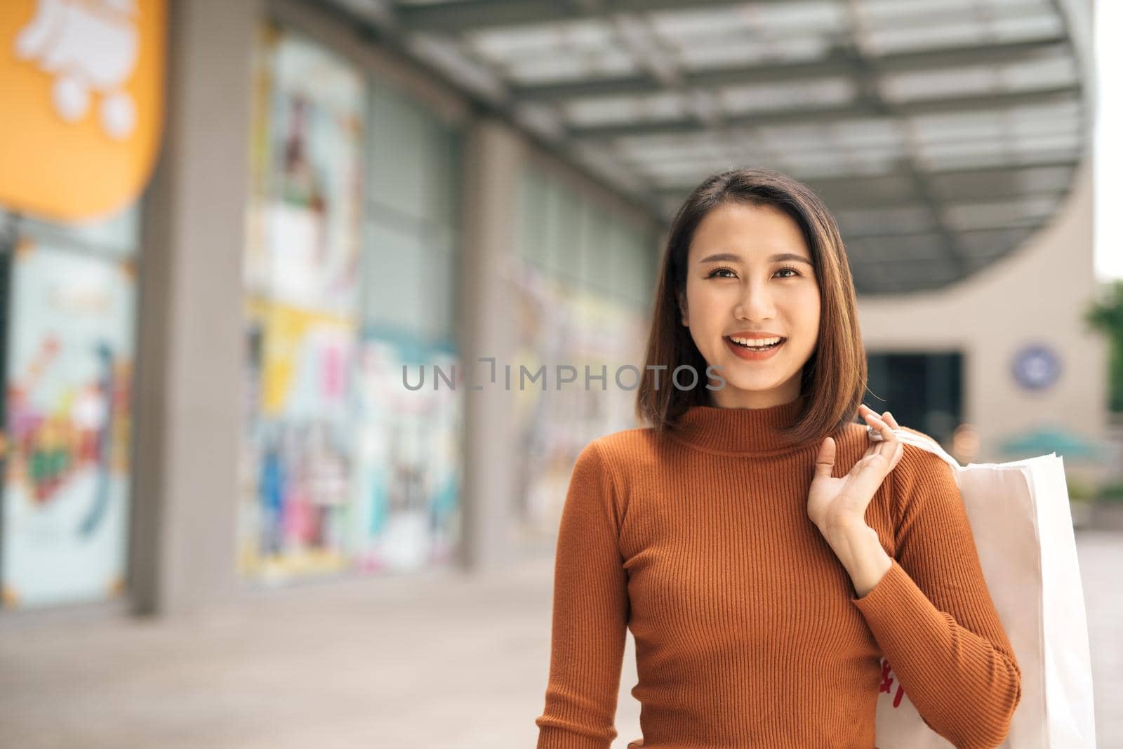 happiness, consumerism, sale and people concept - smiling young Asian woman with shopping bags at outdoor shopping mall