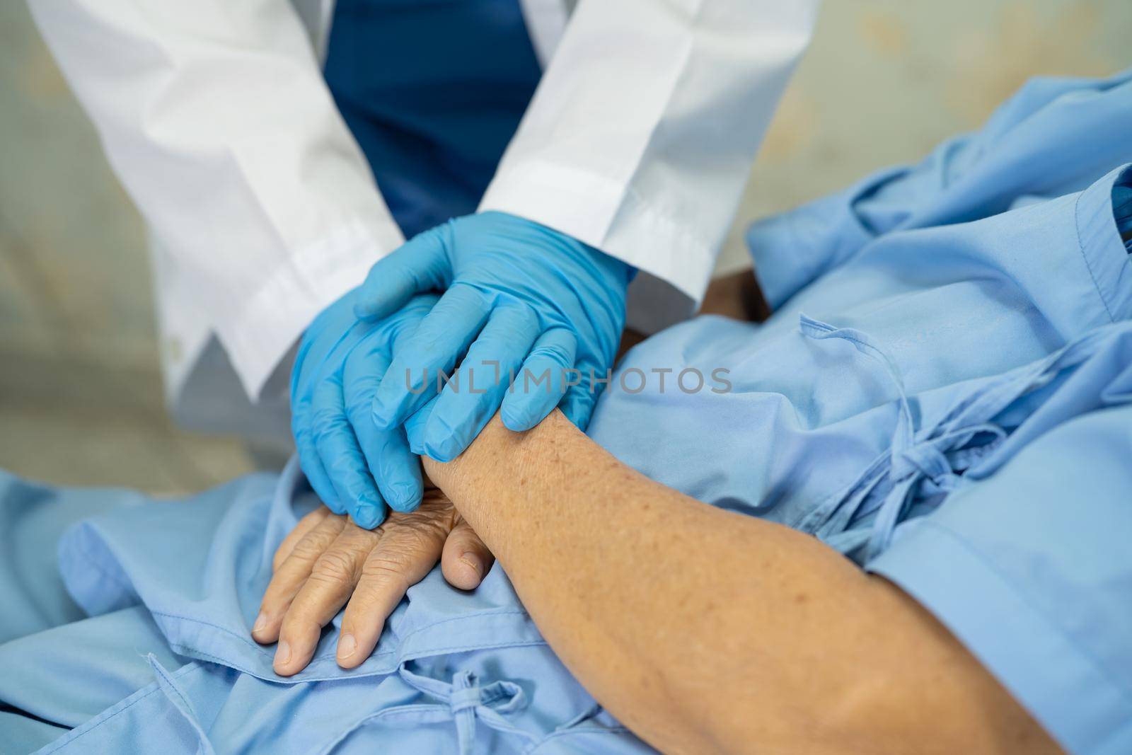 Doctor holding hand and checking Asian senior or elderly old lady woman patient wearing a face mask in hospital for protect infection Covid-19 Coronavirus. by pamai