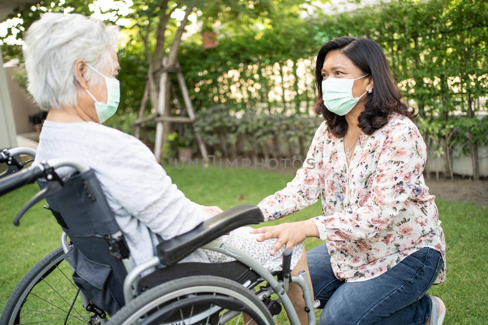 Help Asian senior or elderly old lady woman on wheelchair and wearing a face mask for protect safety infection Covid-19 Coronavirus in park. by pamai