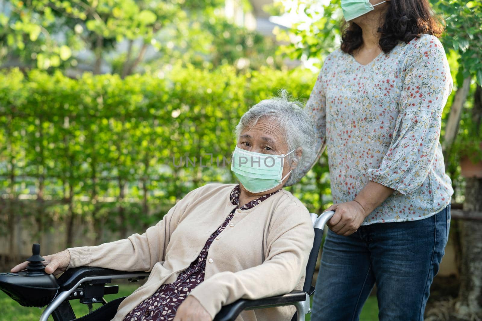 Help Asian senior or elderly old lady woman on electric wheelchair and wearing a face mask for protect safety infection Covid-19 Coronavirus in park. by pamai