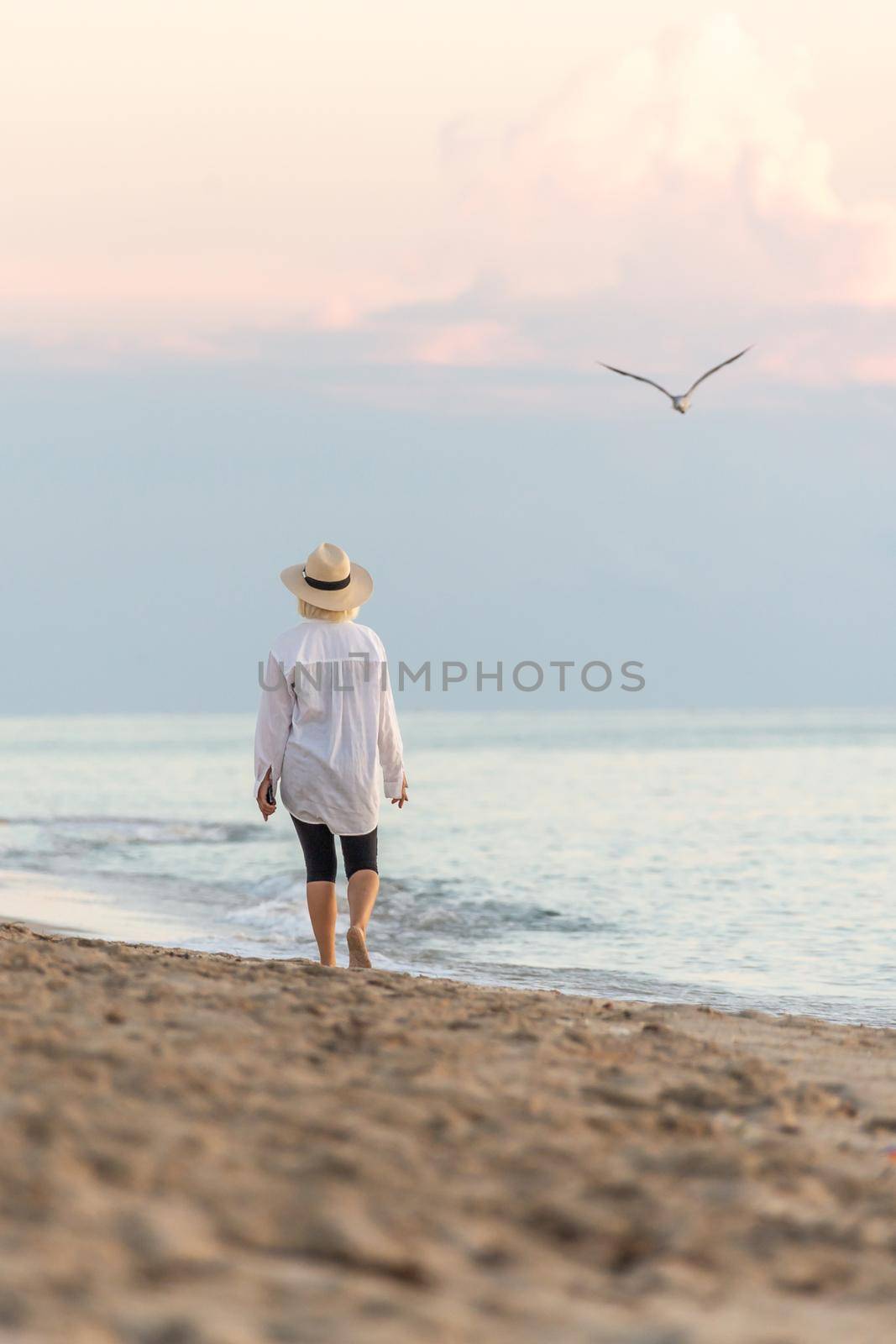 Woman wearing straw hat walking on beach at sunset