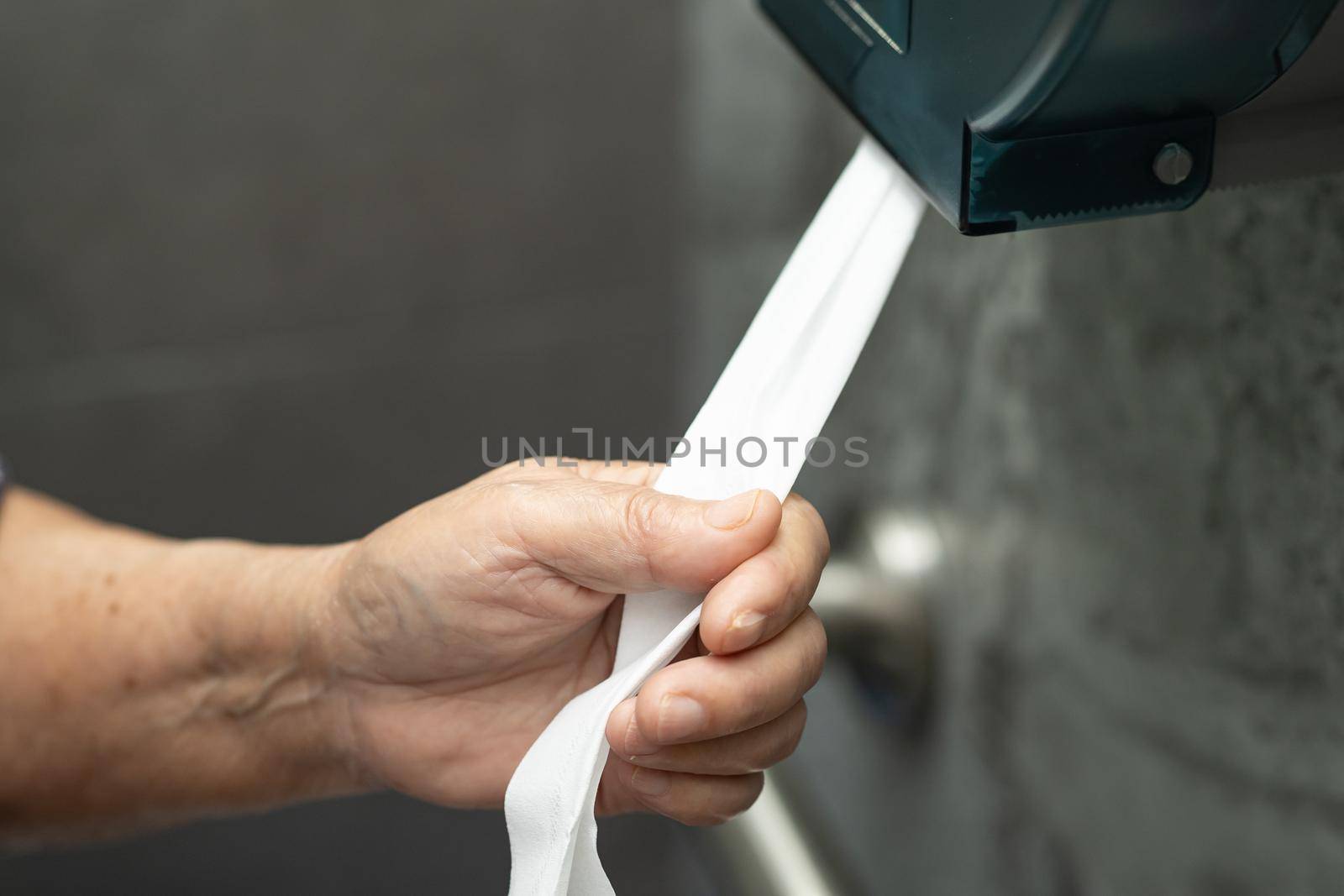 Asian senior elderly old lady woman patient pull the tissue from the roll in toilet bathroom in nursing hospital ward.