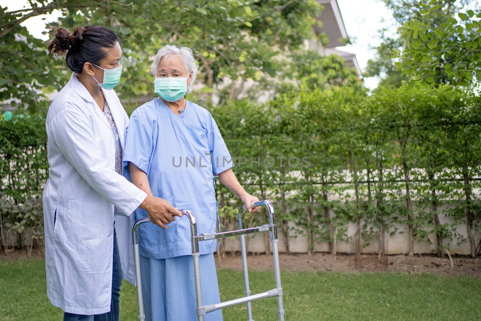 Help and care Asian senior or elderly old lady woman use walker with strong health while walking at park in happy fresh holiday. by pamai