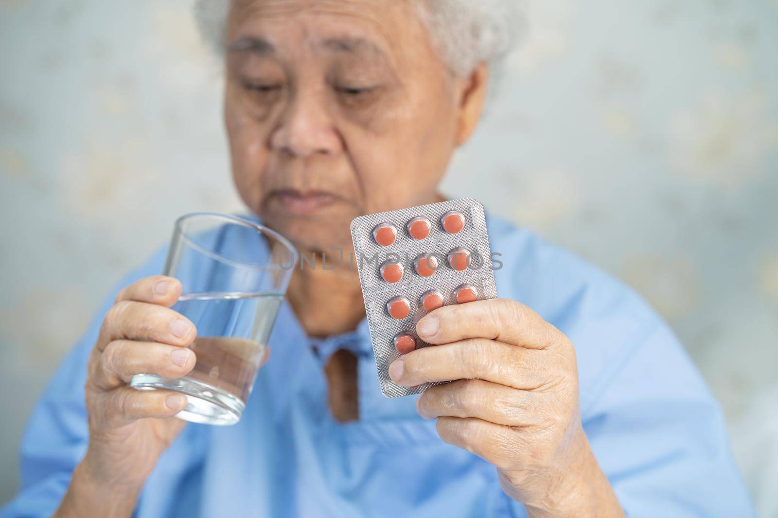 Asian senior or elderly old lady woman patient holding antibiotics capsule pills in blister packaging for treatment infection patient in hospital, Pharmacy drugstore concept. by pamai