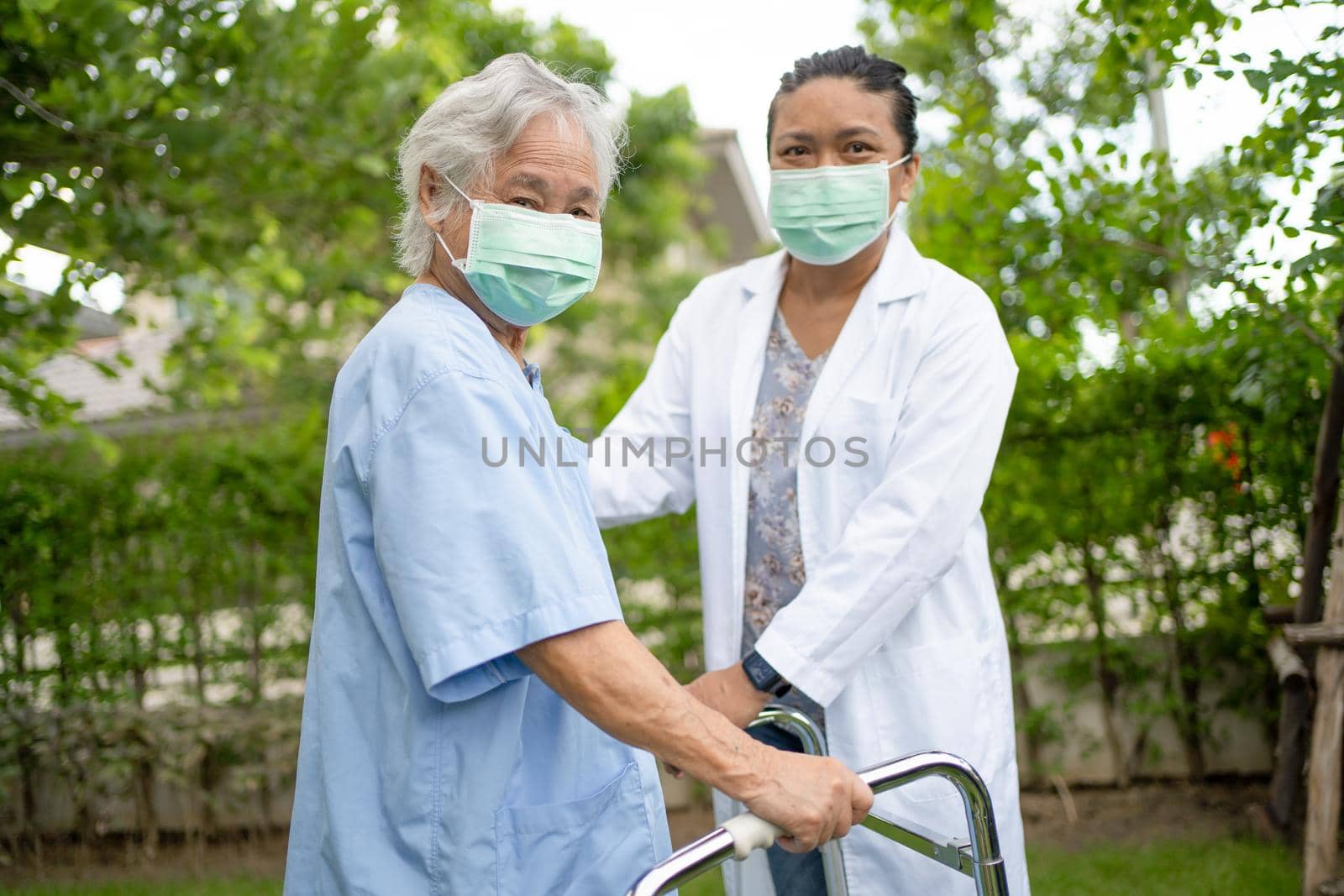 Help and care Asian senior or elderly old lady woman use walker with strong health while walking at park in happy fresh holiday. by pamai