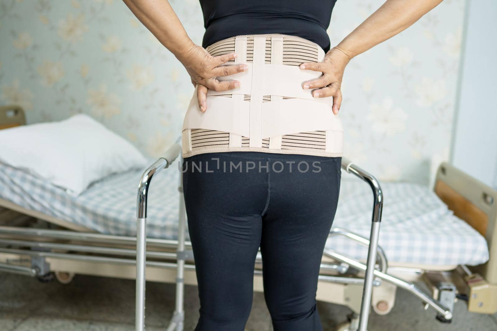 Asian lady patient wearing back pain support belt for orthopedic lumbar with walker. by pamai