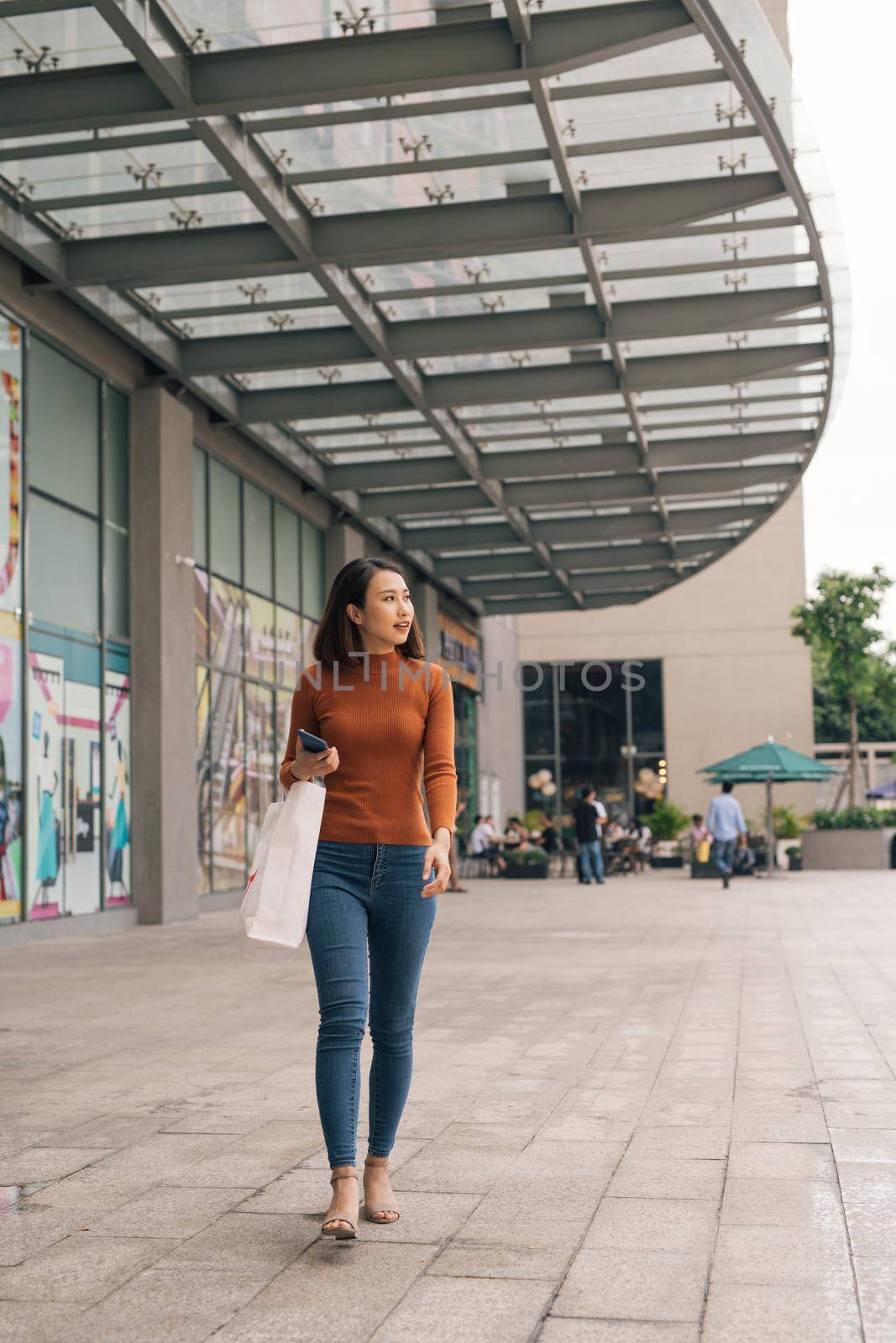 Young happy Asian woman with shopping bags walking on street. by makidotvn