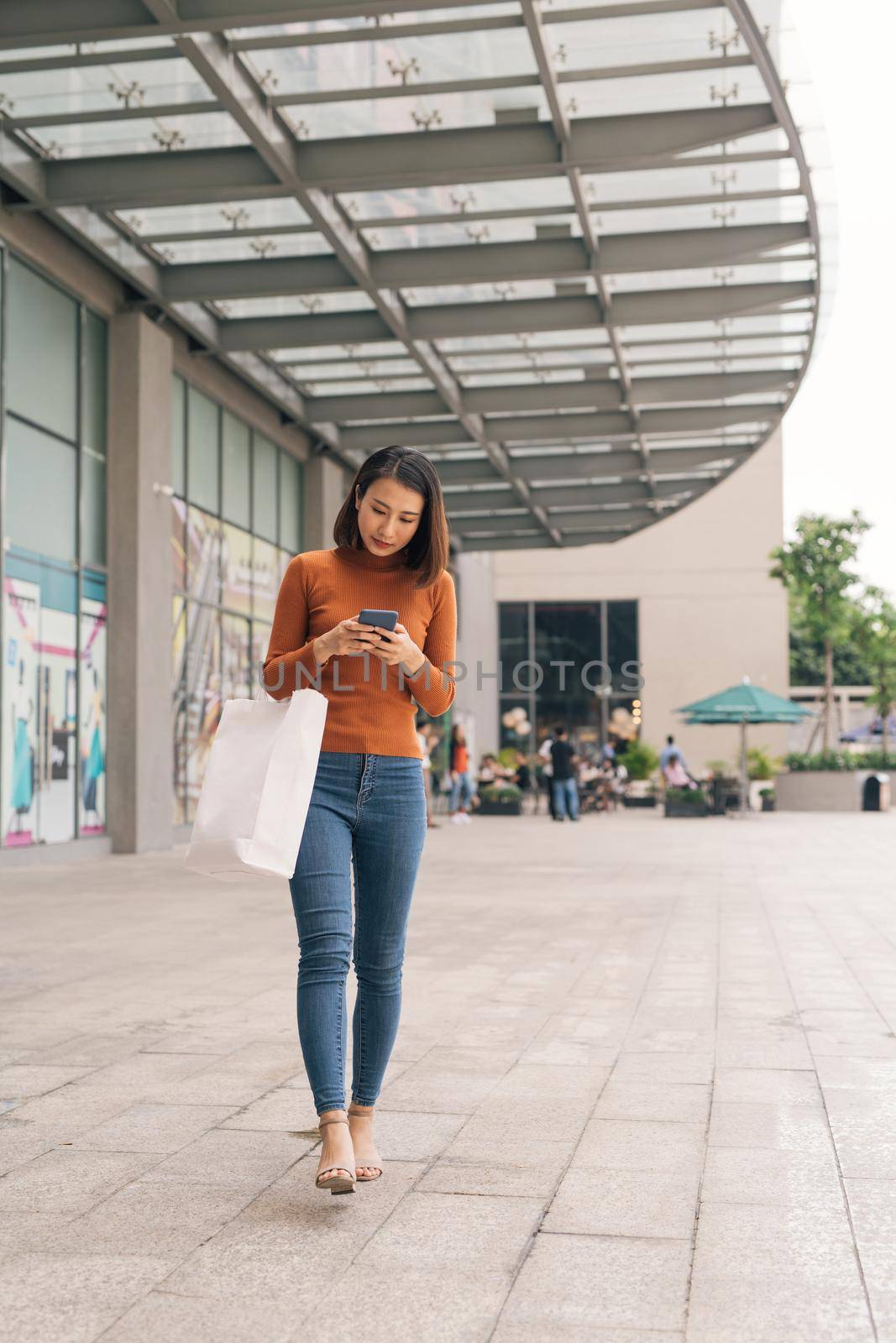 Asian woman go shopping and using mobile phone outdoor shopping mall by makidotvn