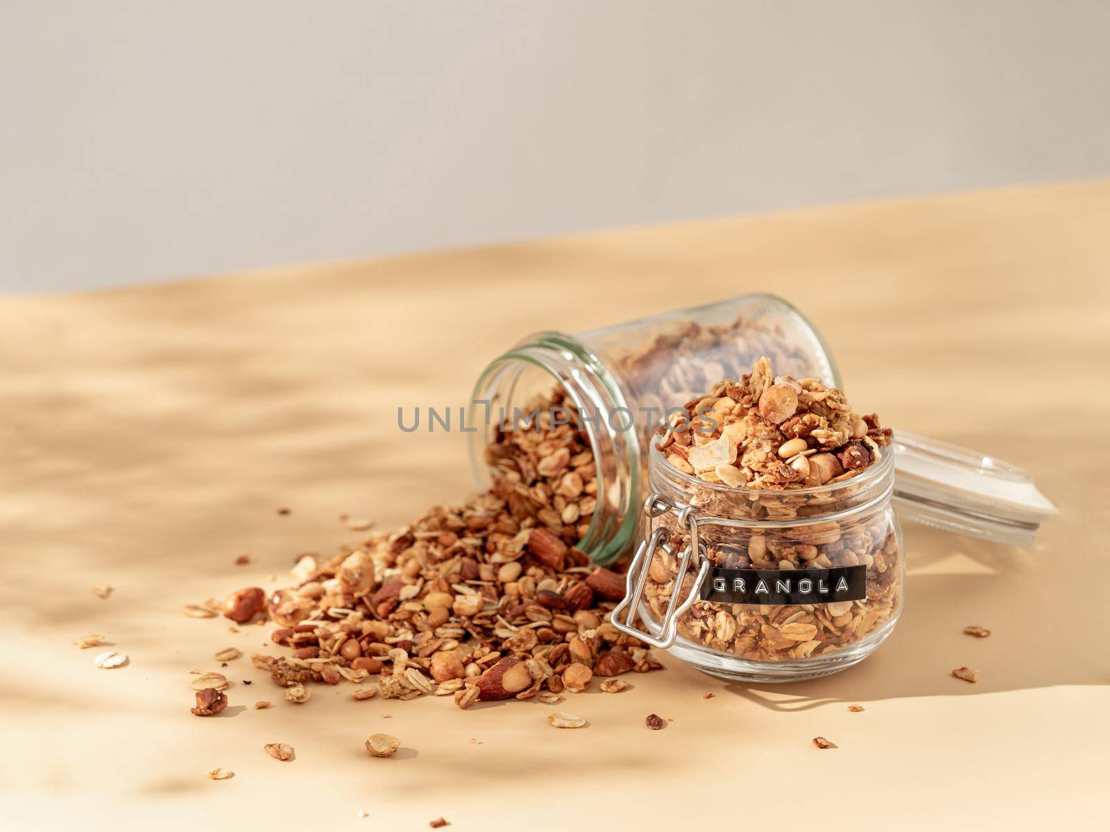 Homemade granola sprinkled of glass jar over pastel beige background. Aesthetic oat granola, beautiful shadows, champagne yellow background. Healthy breakfast concept