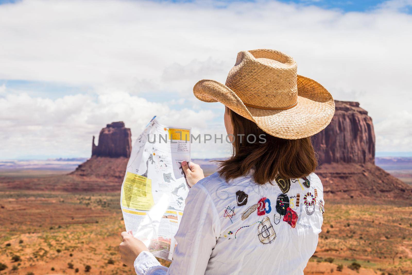 Back side of girl wearing straw hat searching right direction on map in Monument Valley, Utah, USA