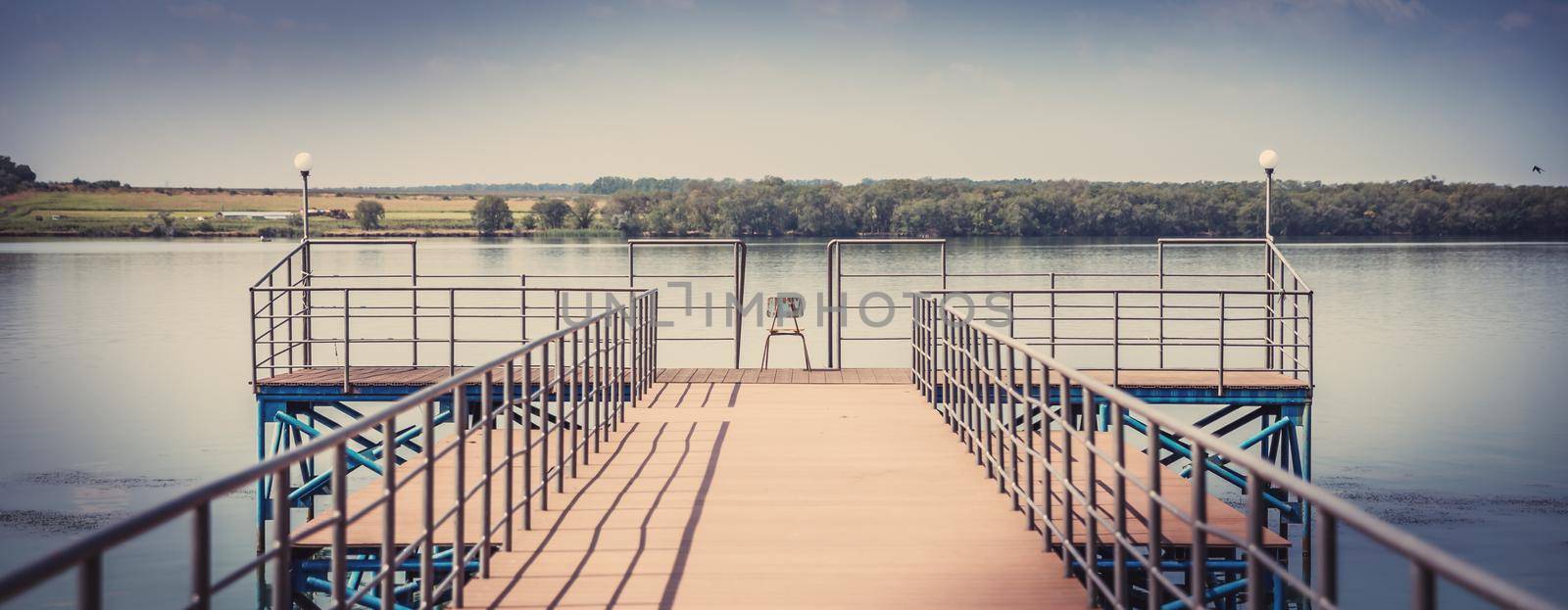 Wooden fishing pier ona beautiful lake with one chair in the middle