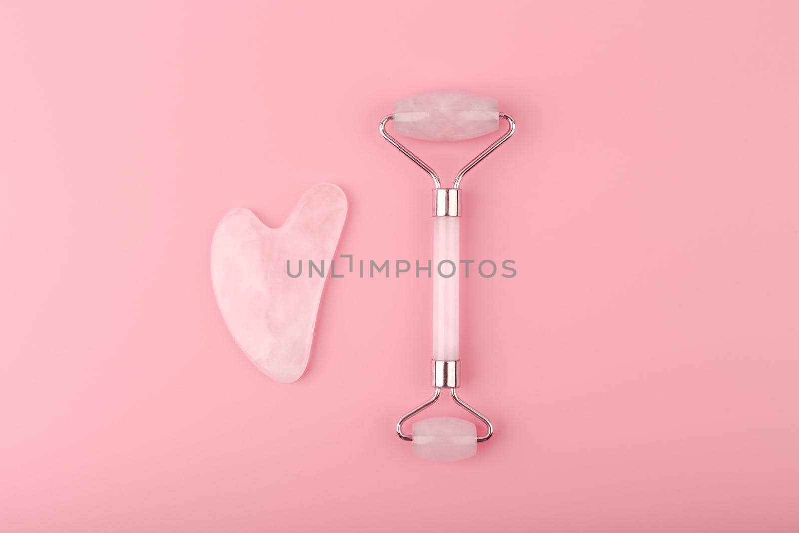 Jade roller and heart shaped guasha scraper massager made of pink quartz on pink background. Concept of self treatment and facial guasha massage for skin lifting and toning