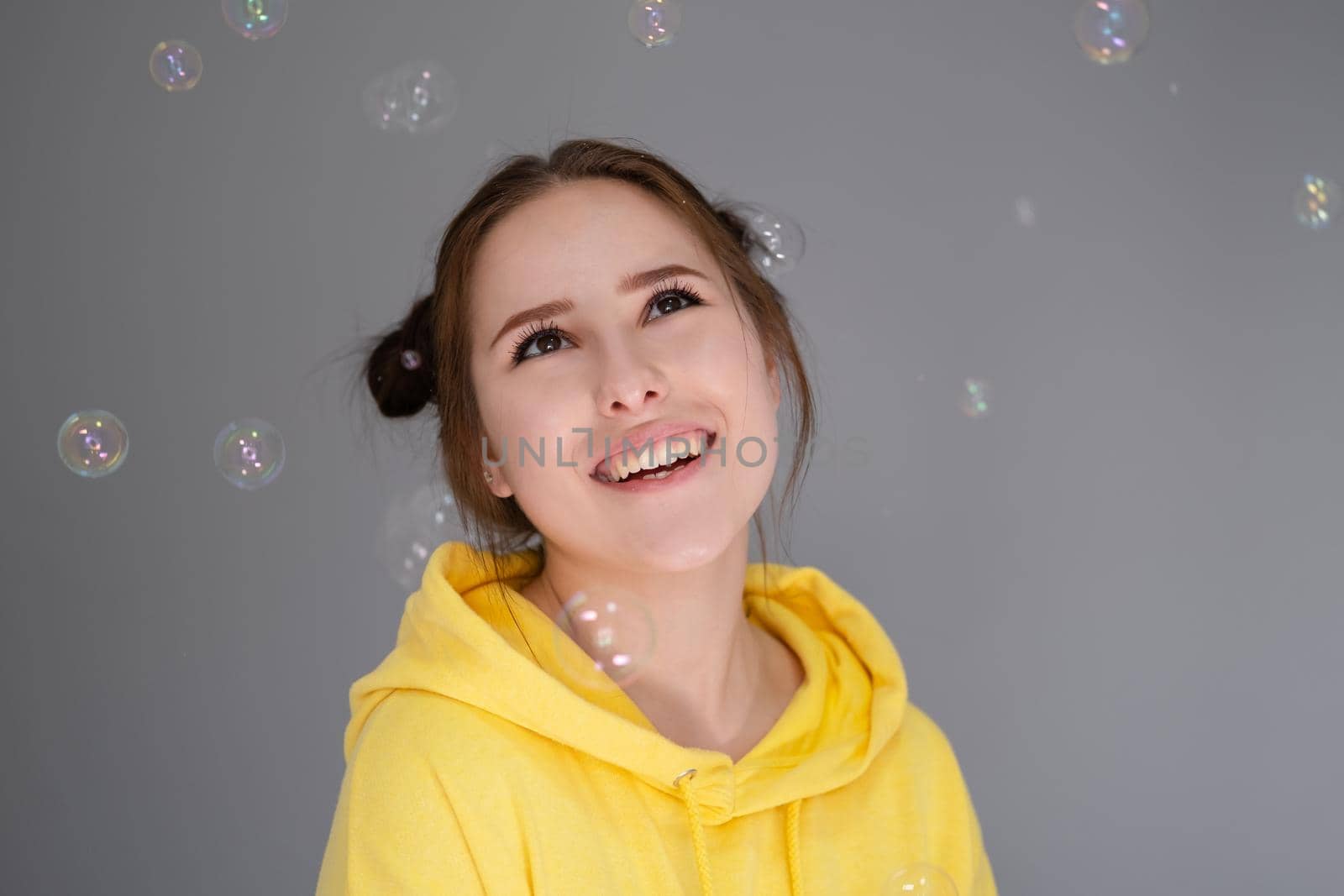 woman in yellow among soap bubbles on grey background.