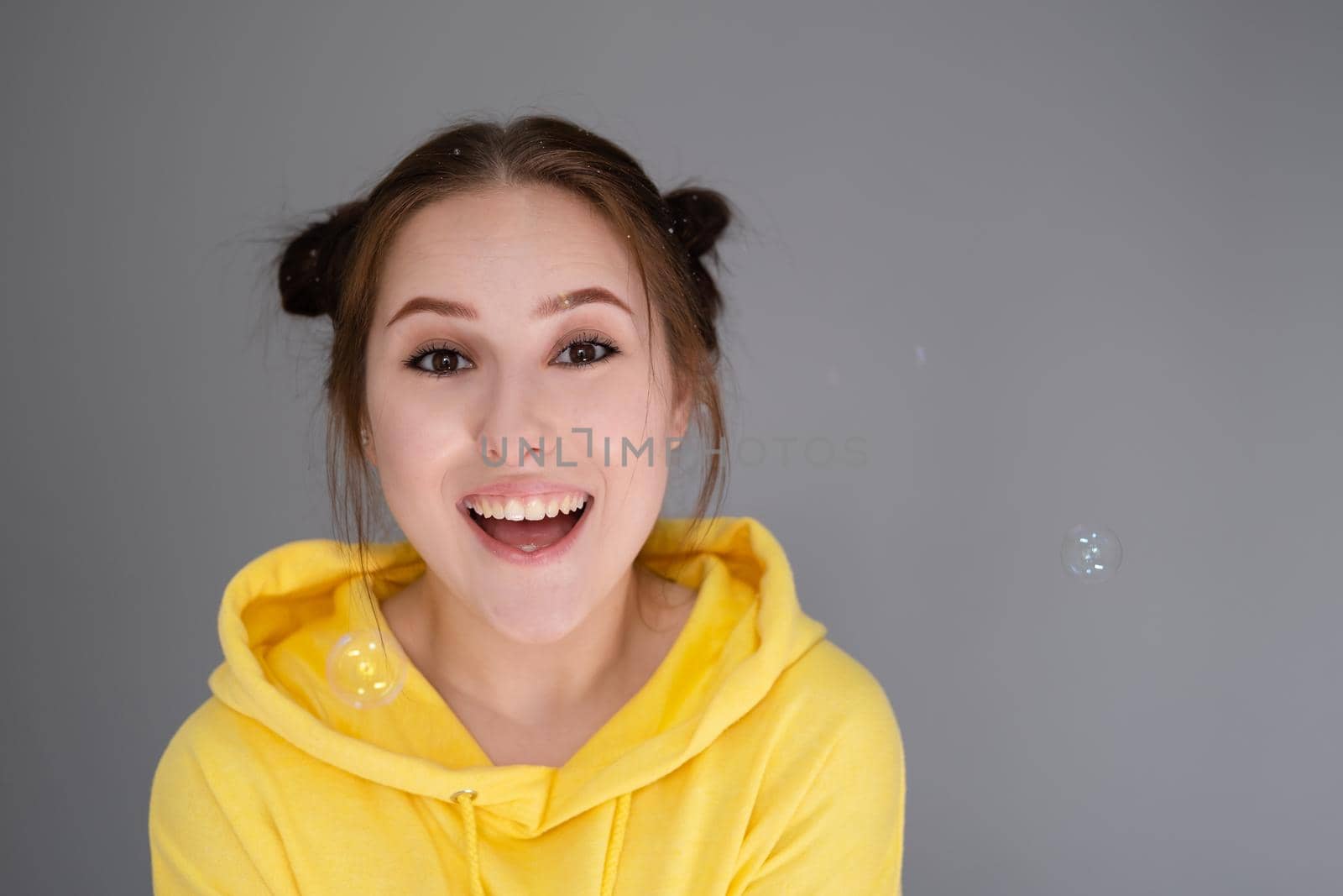 cheerful positive brunette woman in yellow hoodie in white bedroom on bed with white linens. happy people. millennial generation. fashionable teenager.