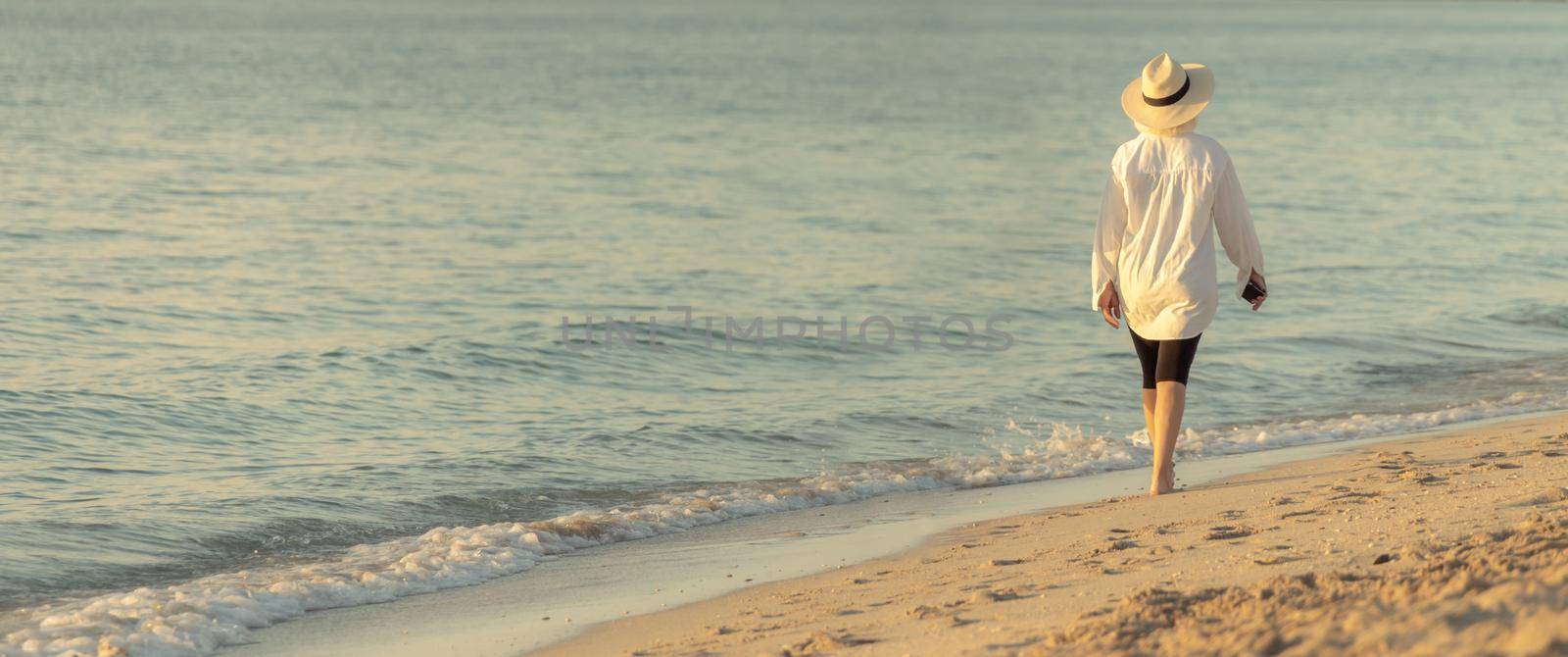 Woman wearing straw hat walking on beach at sunset