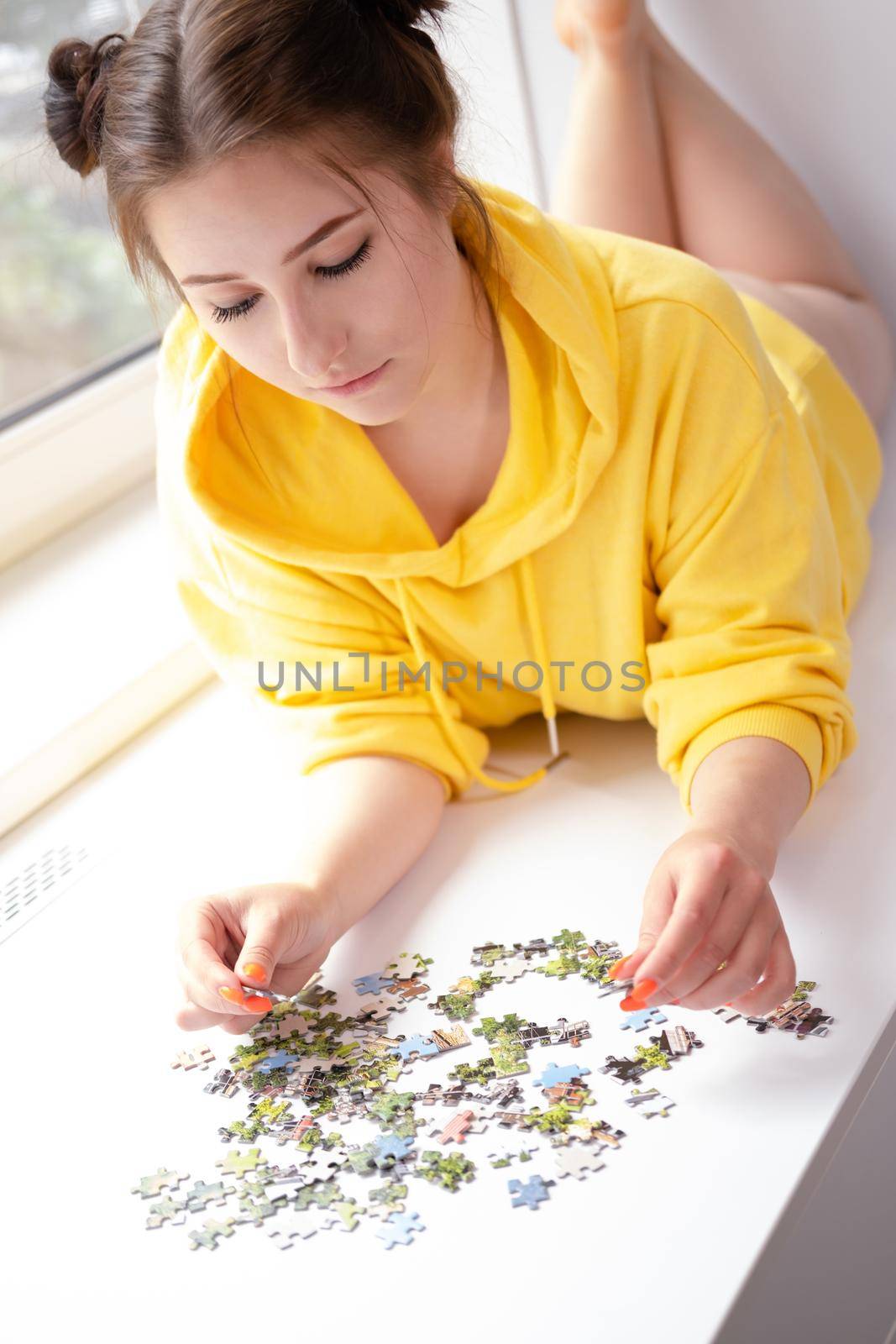 pretty brunette girl in yellow hoodie arranging pieces of a Jigsaw Puzzle Game in bright white room. playing board game home