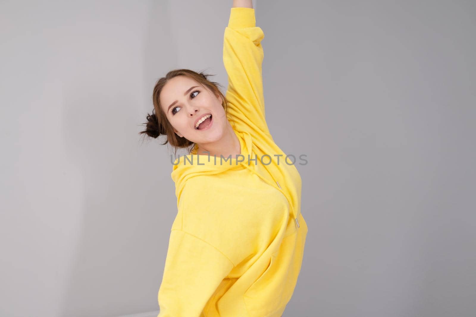 cheerful positive brunette woman in yellow hoodie in white bedroom on bed with white linens. happy people. millennial generation. fashionable teenager.