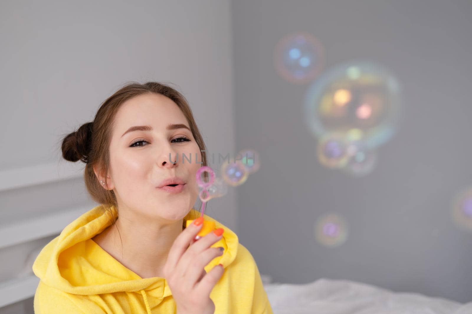 portrait of charming young woman in yellow among soap bubbles on bright grey background. fashionable teenager. trendy colours