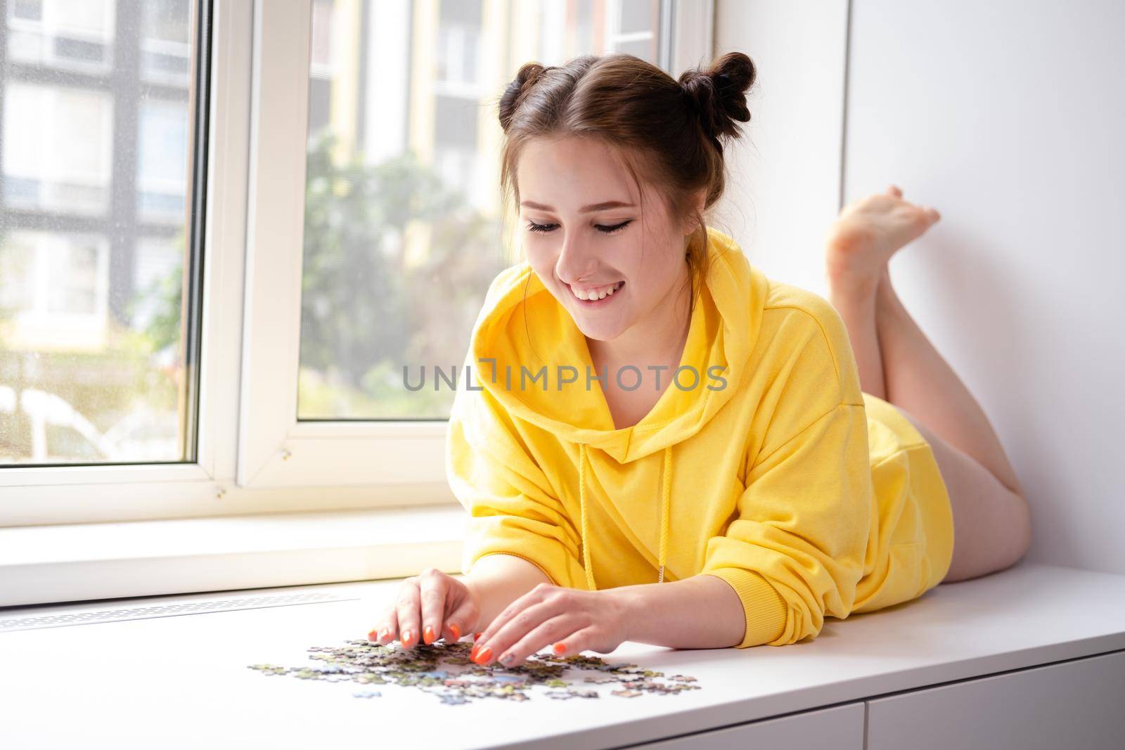 pretty brunette girl in yellow hoodie arranging pieces of a Jigsaw Puzzle Game in bright white room. playing board game home