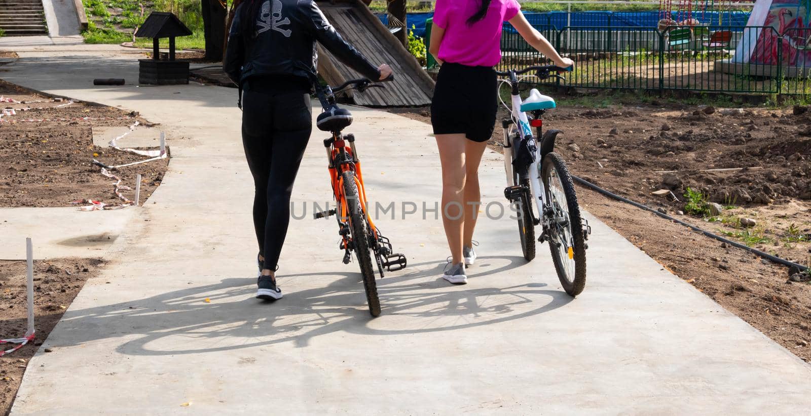 Two young women with bicycles, walking in the city park by lapushka62