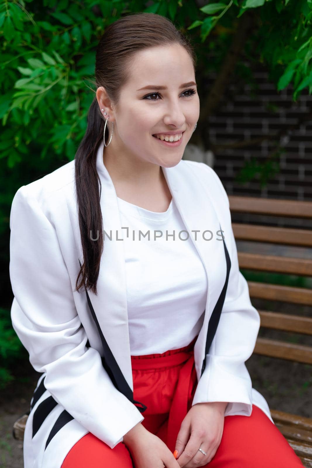 charming young brunette woman in red and white posing outdoors. summertime, green trees.