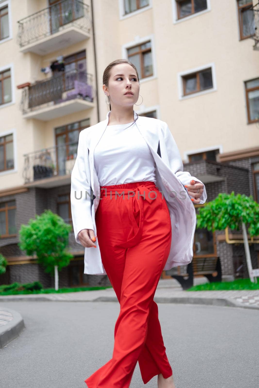 confident brunette woman in red pants and white blouse and jacket walking in the street.