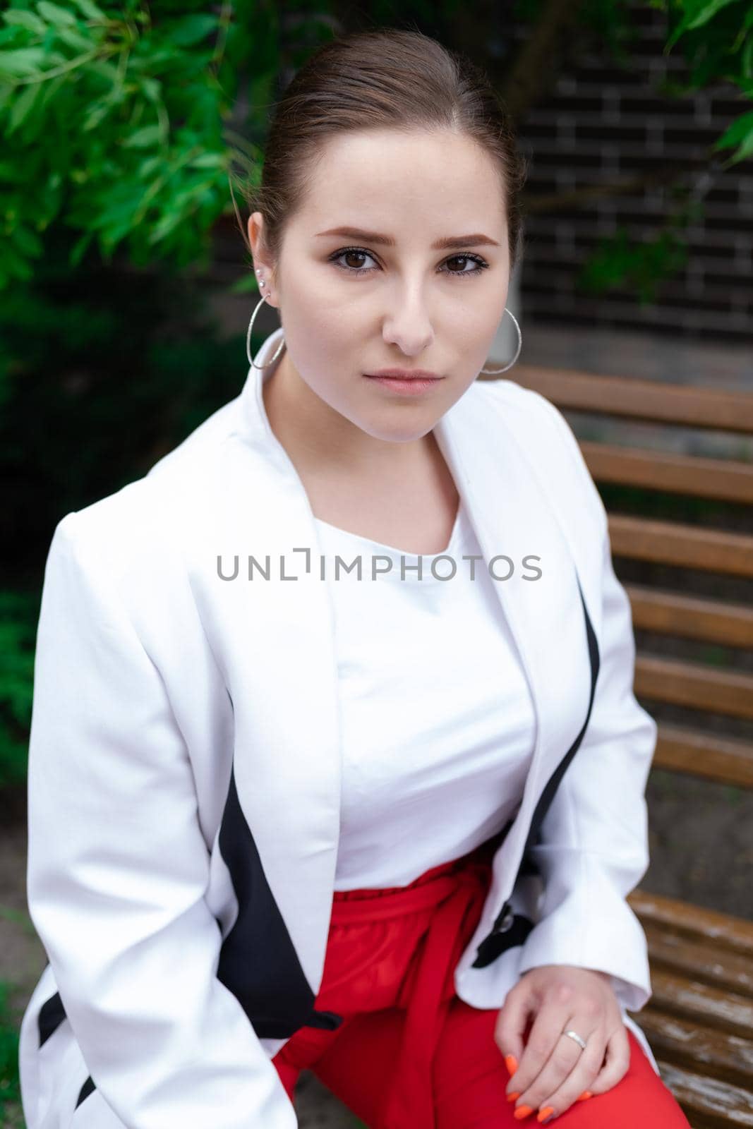 charming young brunette woman in red and white posing outdoors. summertime, green trees.