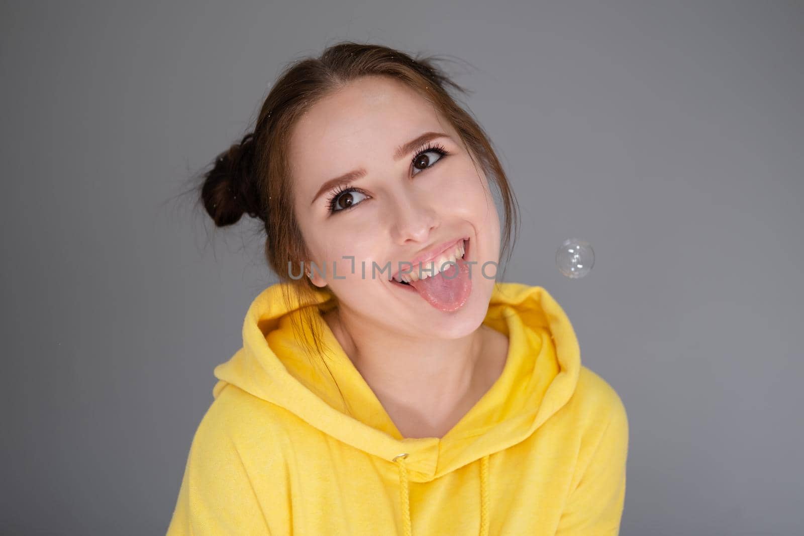 cheerful positive brunette woman in yellow hoodie in white bedroom on bed with white linens. happy people. millennial generation. fashionable teenager.