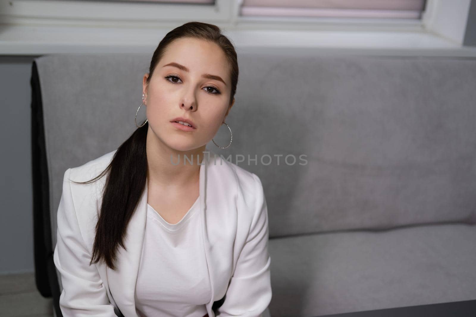 beautiful business woman in red pants, white blouse and Blazer sitting by the table on couch in grey room office.