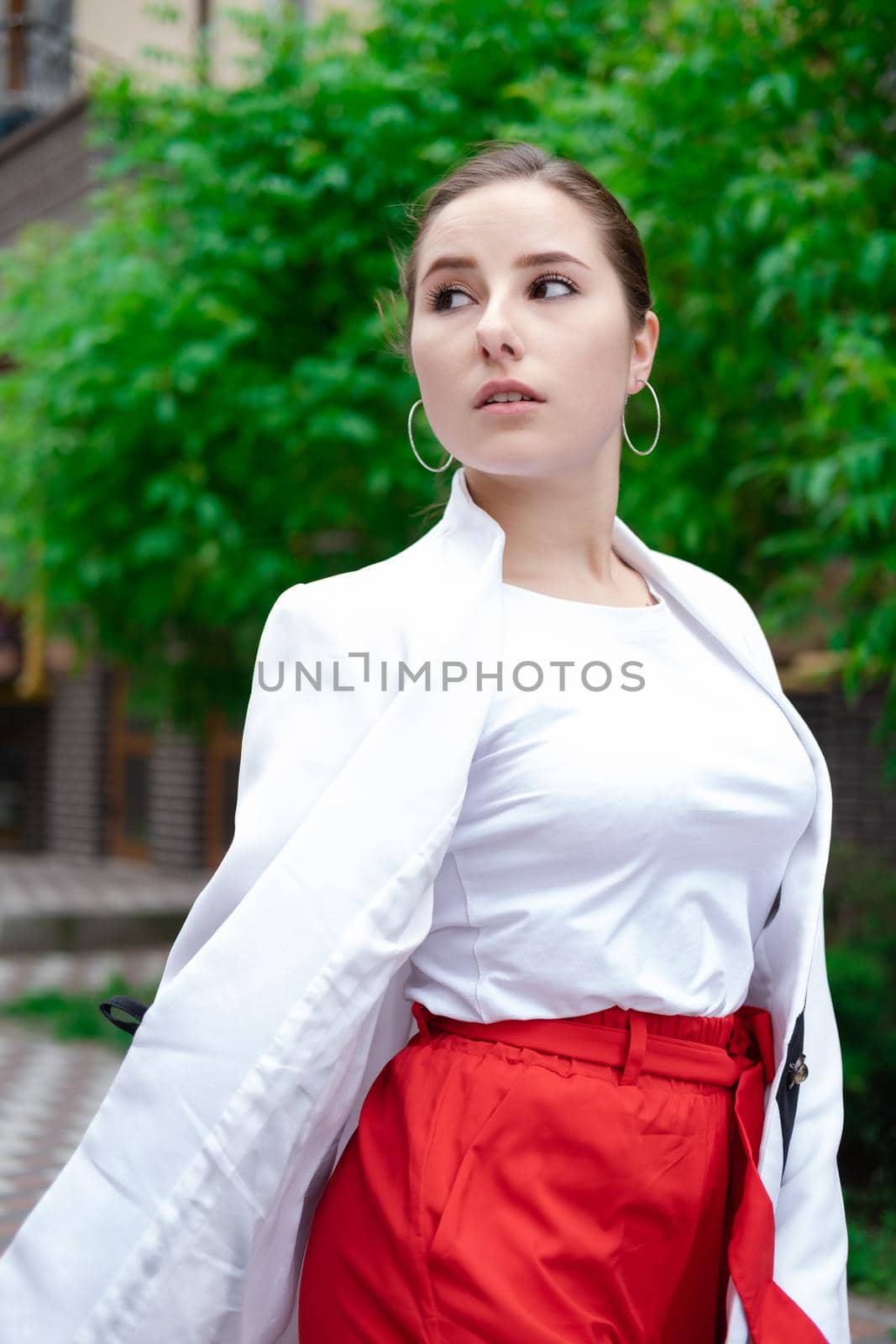 confident brunette woman in red pants and white blouse and jacket walking in the street.