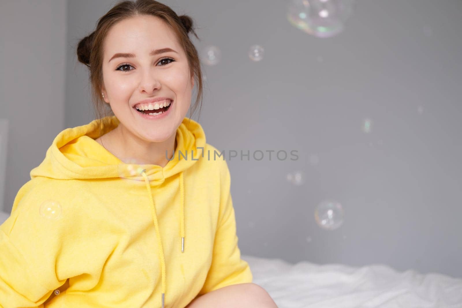 portrait of charming young woman in yellow among soap bubbles on bright grey background. fashionable teenager. trendy colours