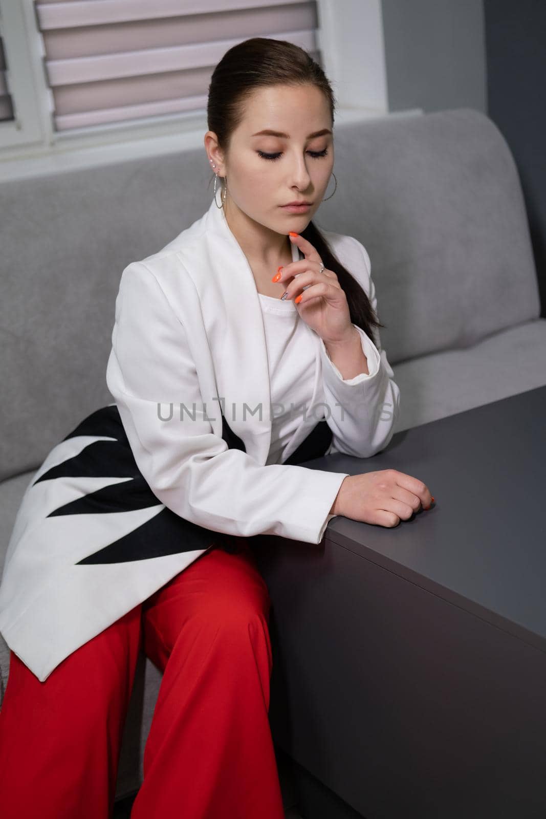 beautiful business woman in red pants, white blouse and Blazer sitting by the table on couch in grey room office by oliavesna